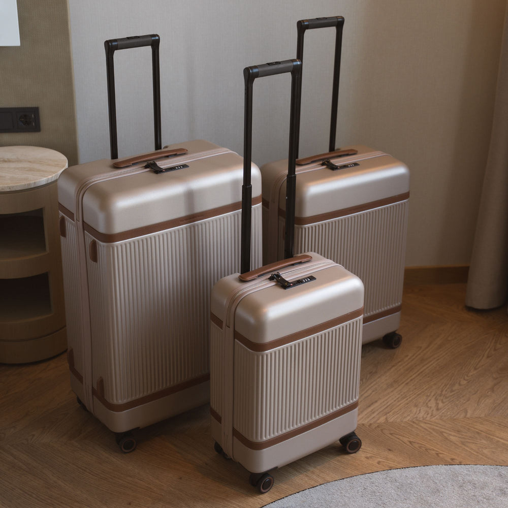 Three beige suitcases with brown accents on a wooden floor.