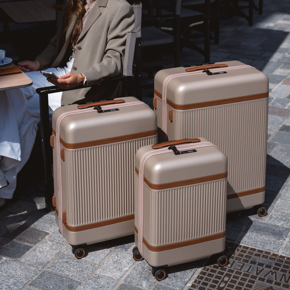 Set of three beige suitcases with brown accents on a stone pavement.