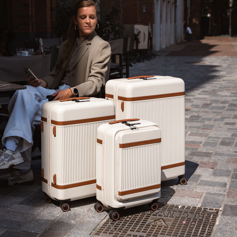 Woman sitting on a bench with three white suitcases featuring brown accents.