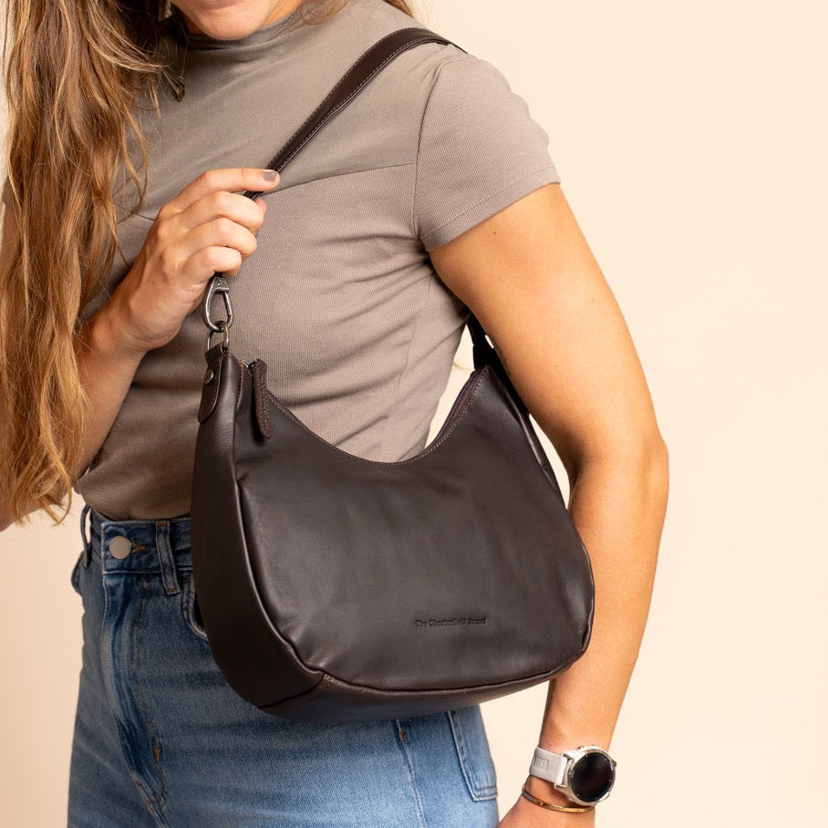 Woman holding a brown shoulder bag against a beige background