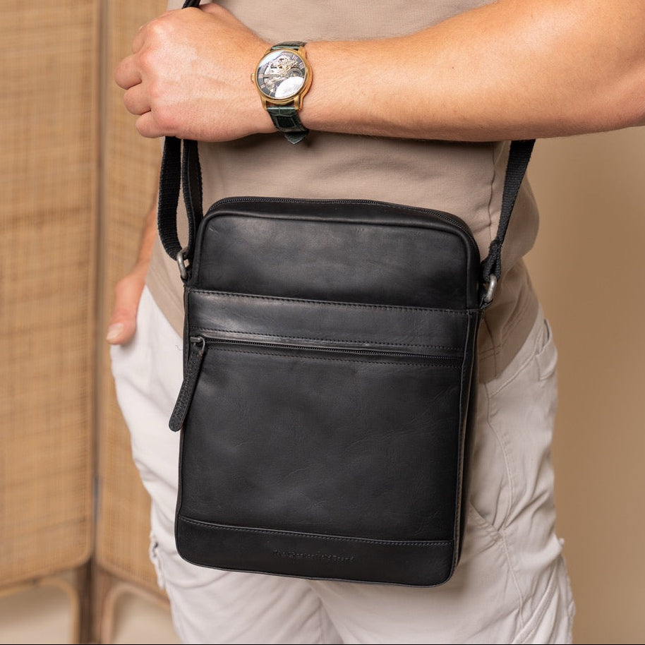 Person wearing a black crossbody bag with a neutral background