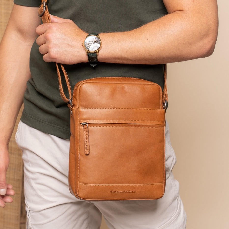 Person holding a cognac leather crossbody bag against a beige background