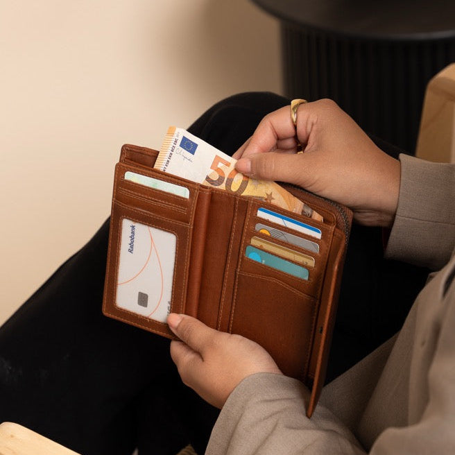 Person sitting on a chair holding a cognac wallet with cards, wearing a beige coat.