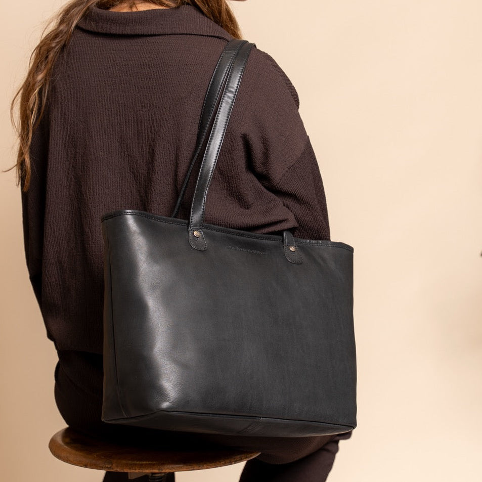 Person holding a black leather tote bag against a beige background