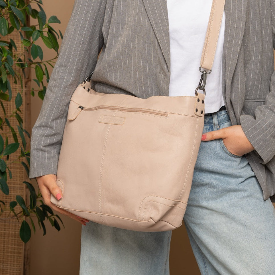 Person wearing a gray pinstripe blazer and light blue jeans, holding a beige shoulder bag against a beige background.