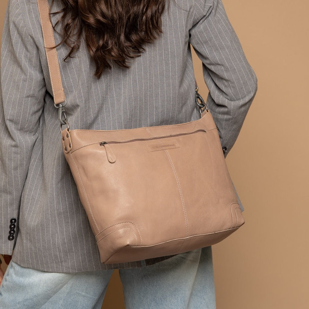 Person wearing a beige shoulder bag against a brown background