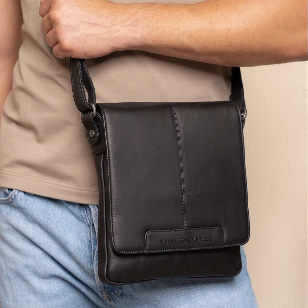 Person wearing a black leather crossbody bag with a neutral background