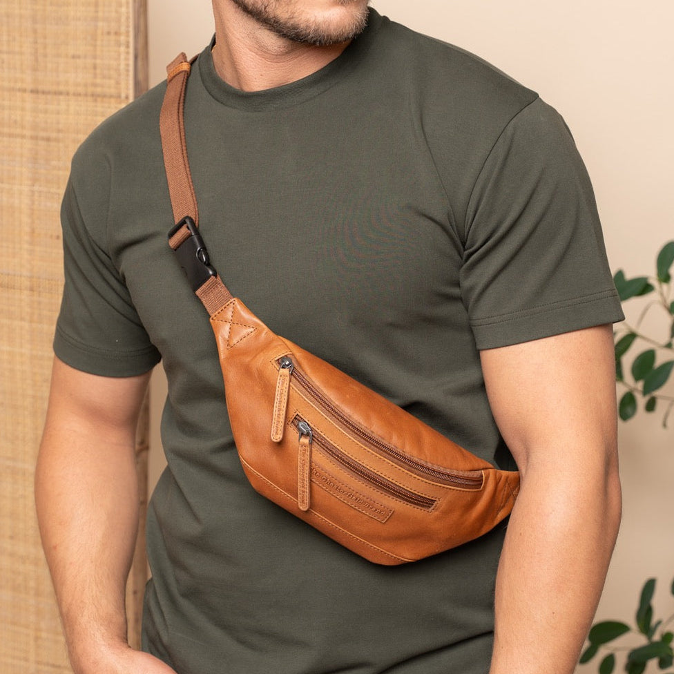 Man wearing a green t-shirt with a cognac leather waist bag against a beige wall.