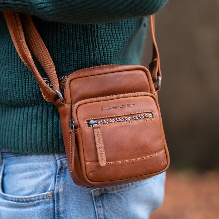 Person wearing a cognac leather crossbody bag with a blurred natural background