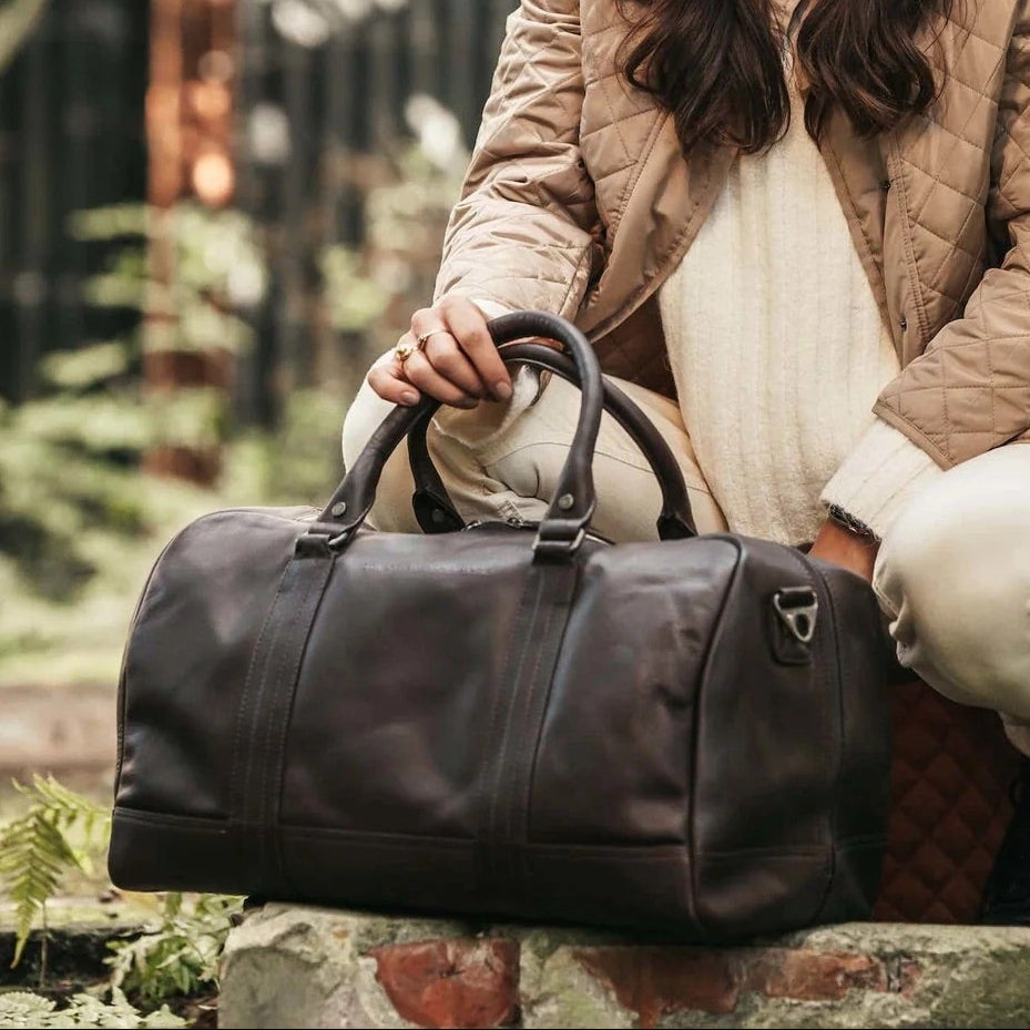 Woman holding a black leather duffel bag in an outdoor setting.