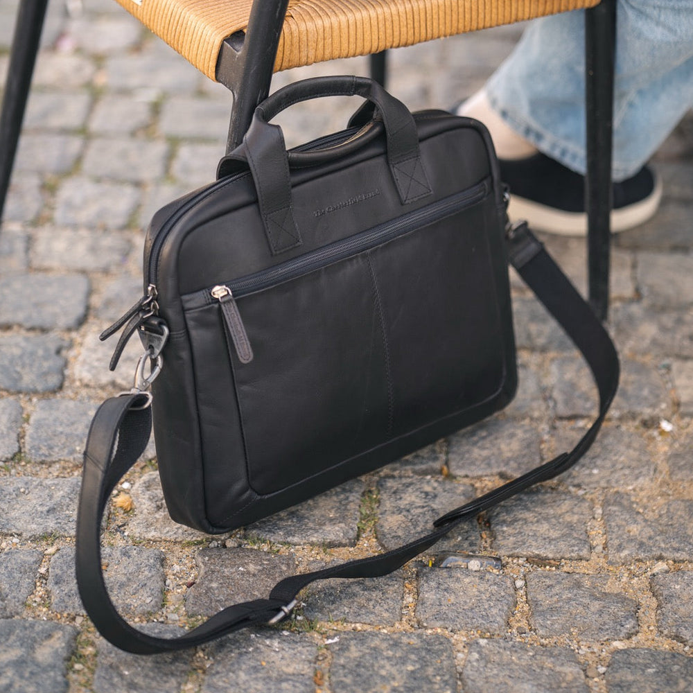 Black briefcase on a cobblestone street with a person sitting on a chair in the background.