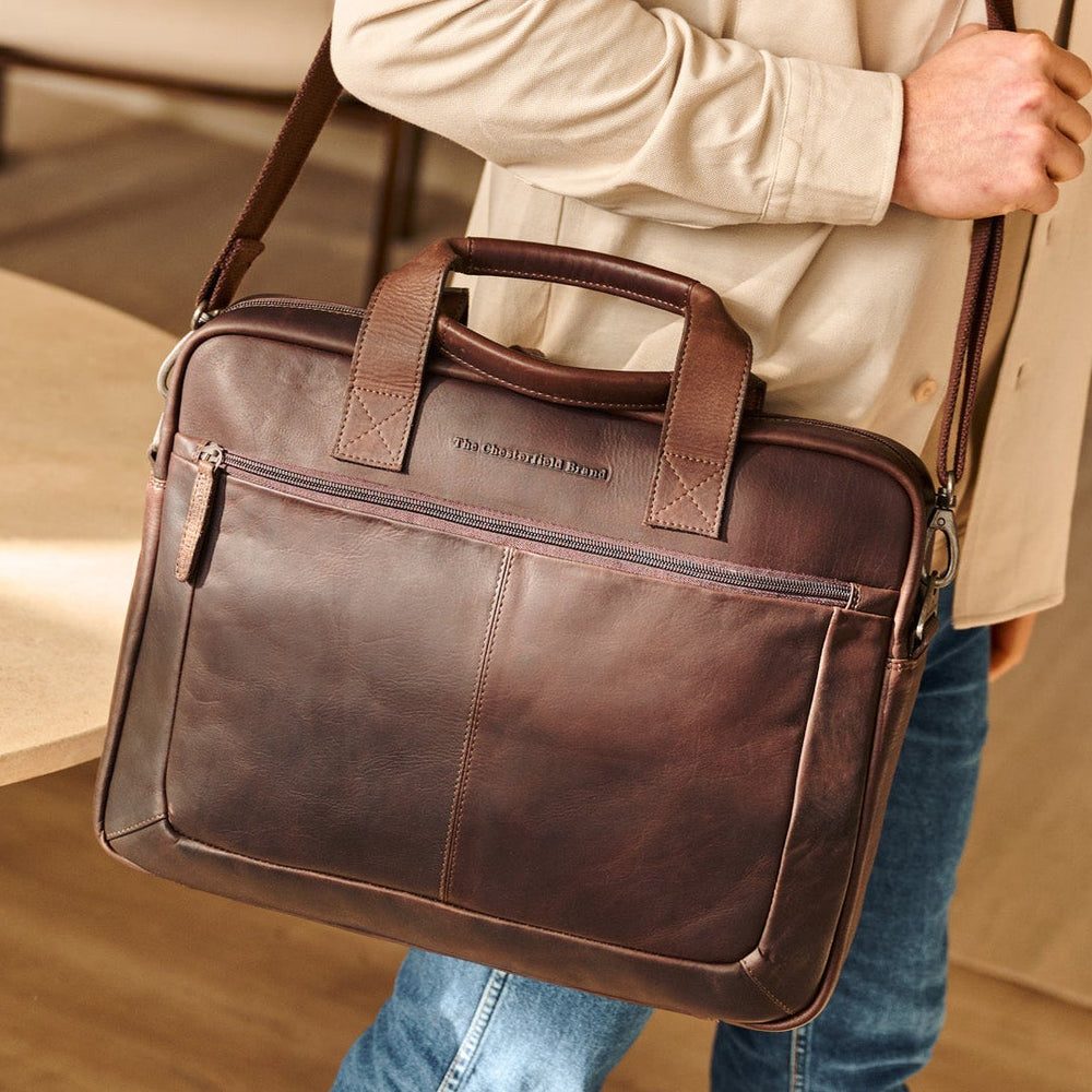 Person holding a brown leather briefcase in an indoor setting