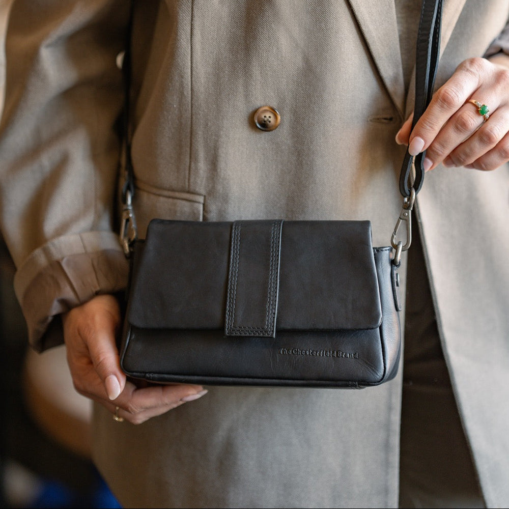 Person holding a black leather crossbody bag with a blurred background