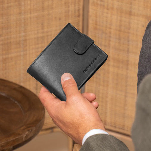 Man holding a black wallet next to a beige vase on a wooden table against a woven wall.