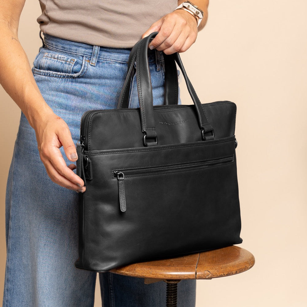 Person holding a black leather laptop bag on a beige background