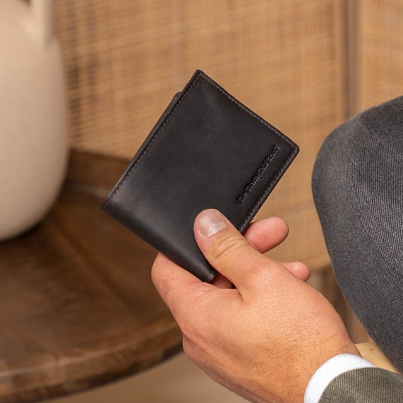 Person holding a brown wallet with a vase and chair in the background