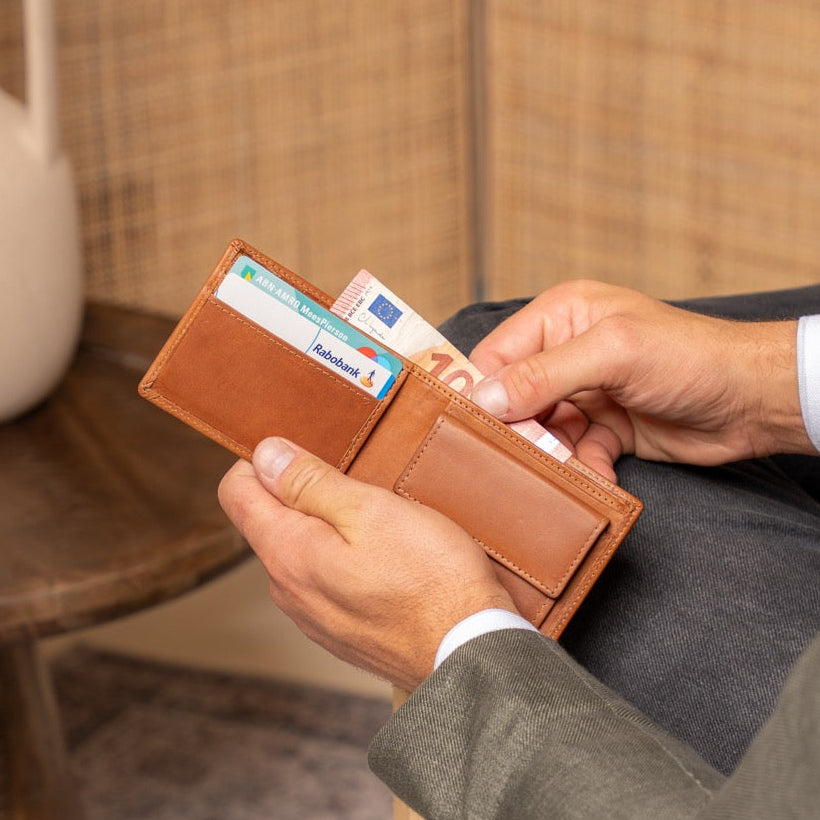 Person holding a cognac wallet with cards, sitting on a wooden chair.
