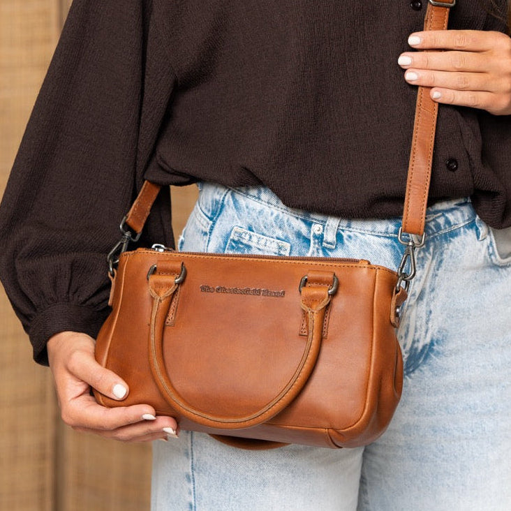 Person holding a cognac leather handbag against a beige wall.