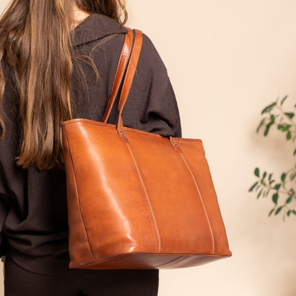 Person carrying a cognac leather tote bag with a neutral background