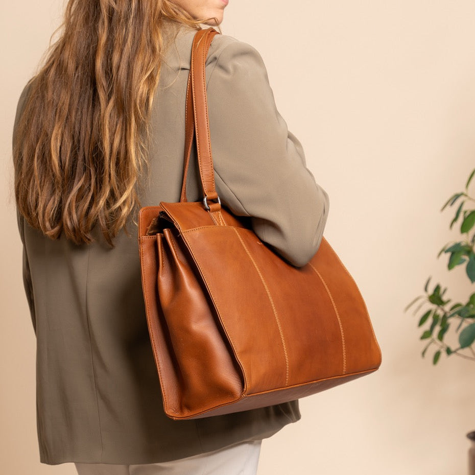 Woman holding a cognac leather bag against a beige background
