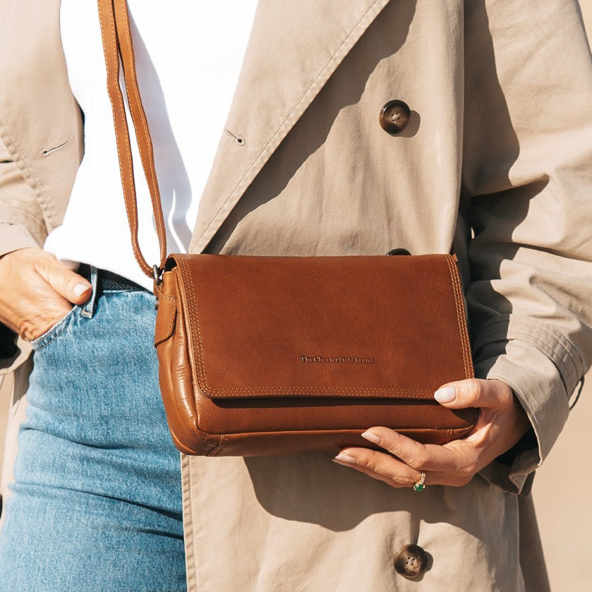 Person holding a cognac leather bag against a neutral background