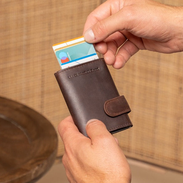 Person holding a brown wallet with a card, sitting on a couch with a vase in the background