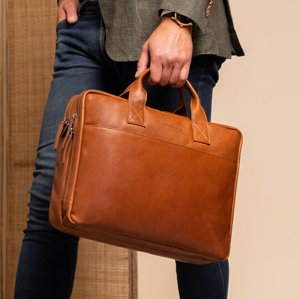 Person holding a cognac leather briefcase against a neutral background