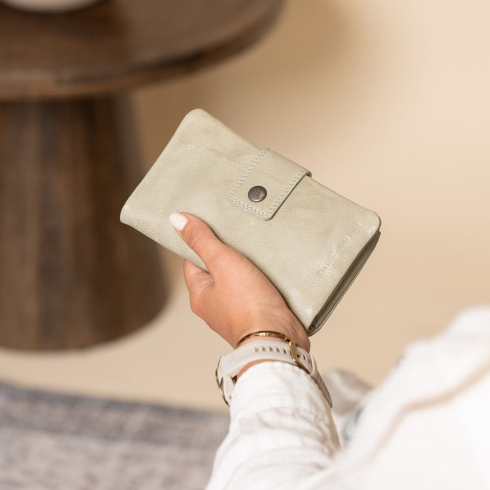 Person holding a soft green wallet in a home setting
