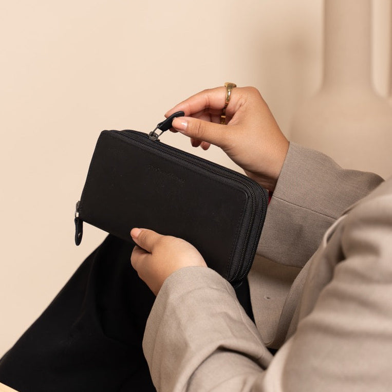 Person sitting in a chair holding a black pouch against a neutral background