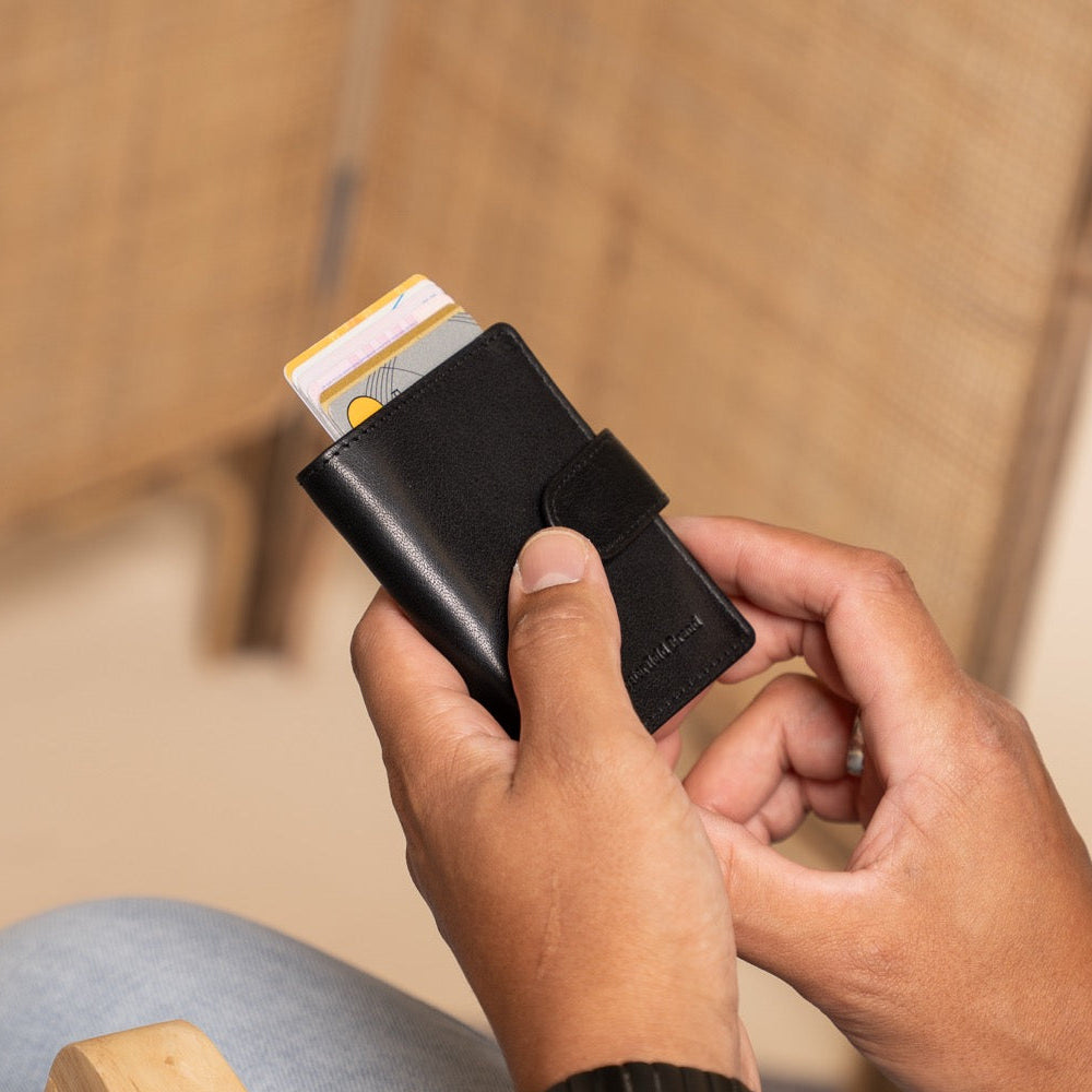 Person holding a black wallet with cards, sitting on a wooden chair.
