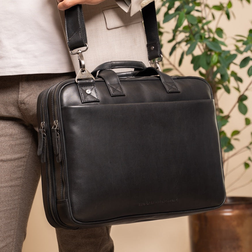 Person holding a black leather business bag with a plant in the background