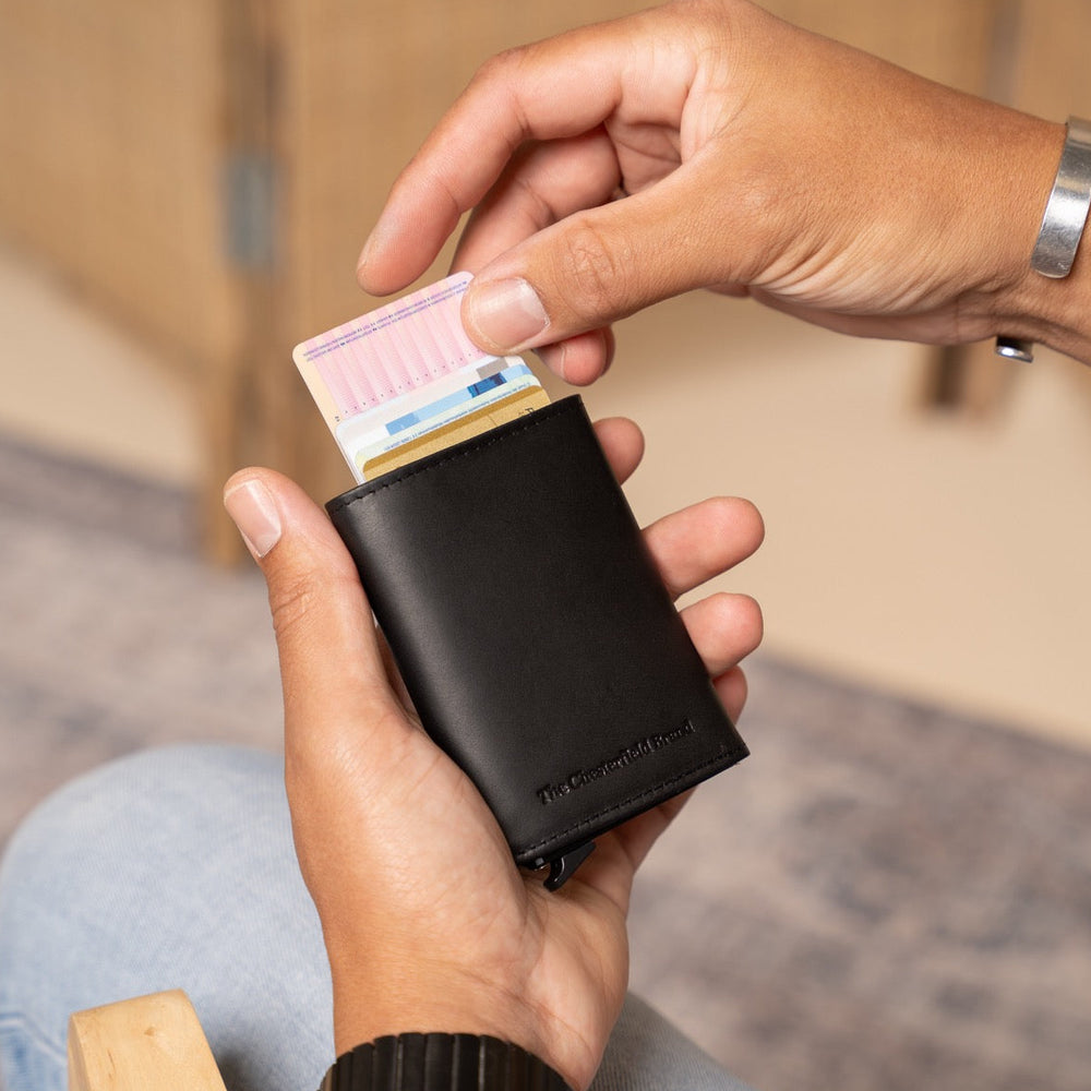 Person holding a black wallet with a card and money, blurred background