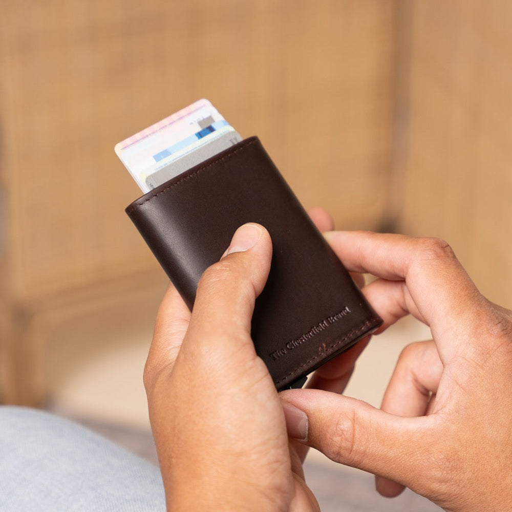 Person holding a brown wallet with cards against a blurred background