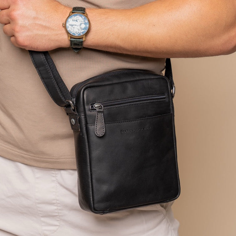 Person wearing a black crossbody bag and beige shirt on a beige background