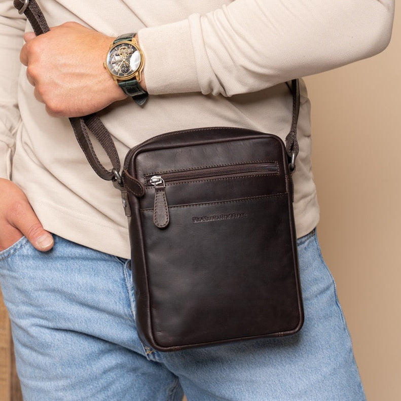 Person wearing a beige sweater and blue jeans with a brown crossbody bag on a beige background