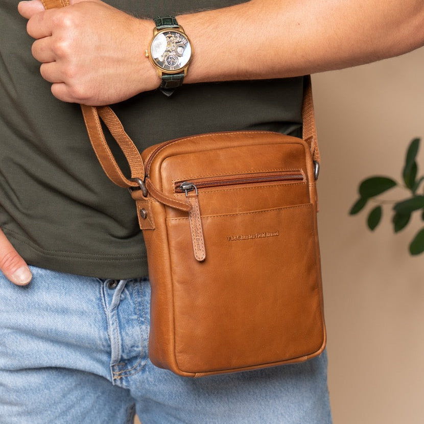 Person holding a cognac leather crossbody bag with a blurred background