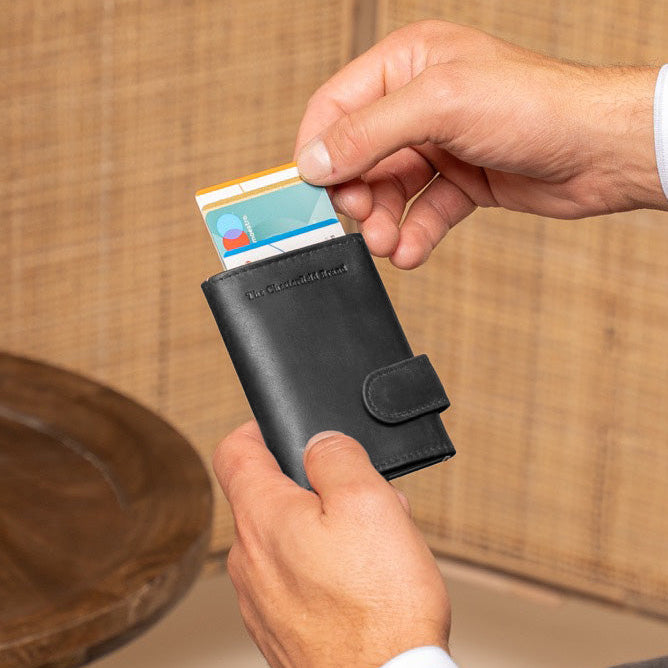 Person holding a black wallet with a card, sitting on a couch with a vase in the background
