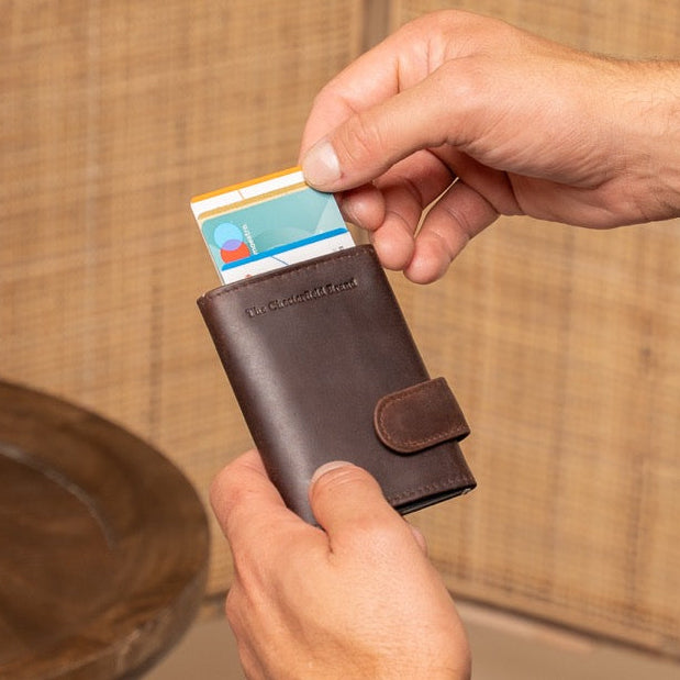 Person holding a brown wallet with a card, sitting on a couch with a vase in the background
