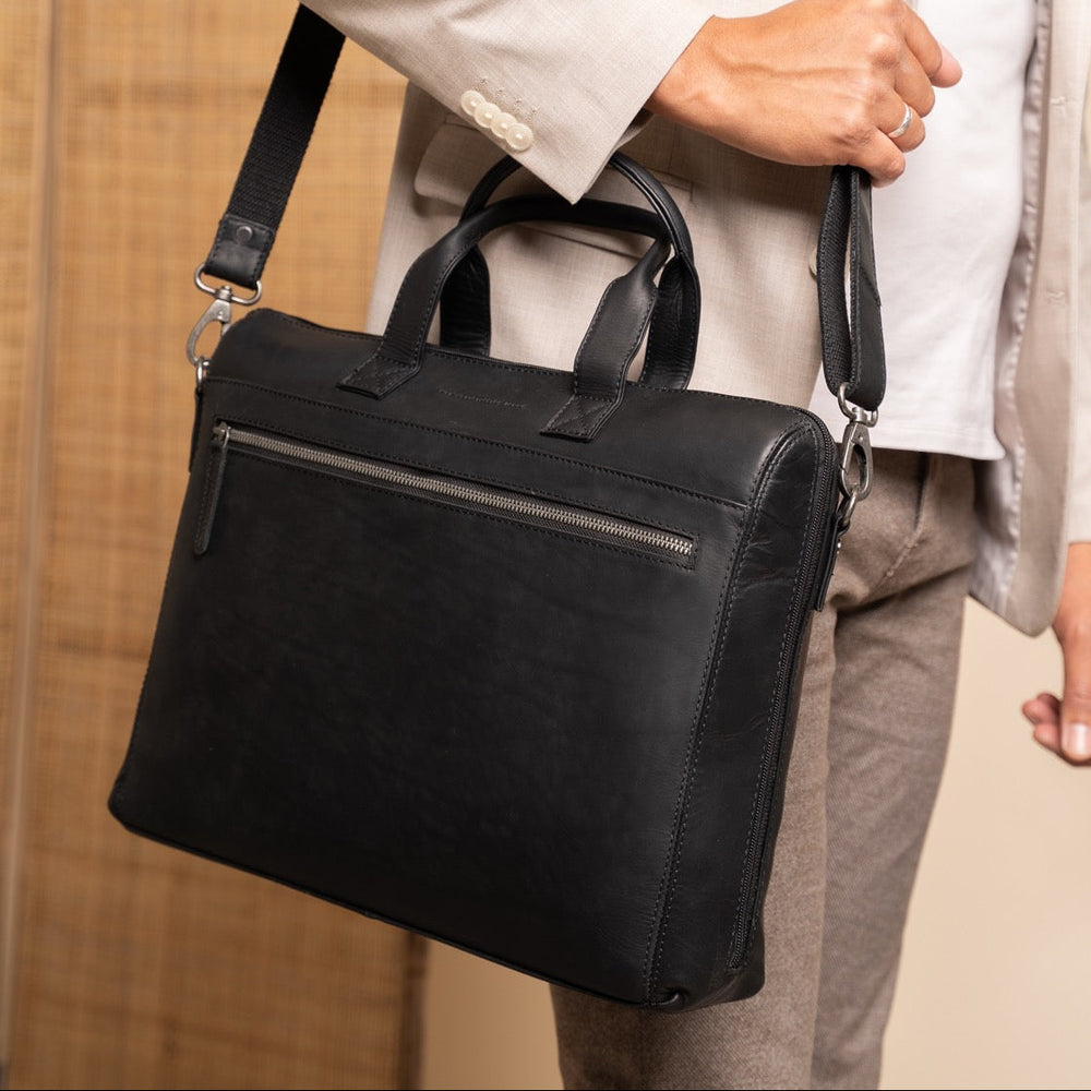 Person holding a black leather briefcase with a blurred background