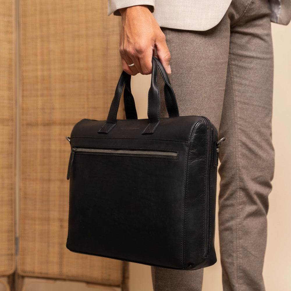 Person holding a black leather briefcase against a neutral background