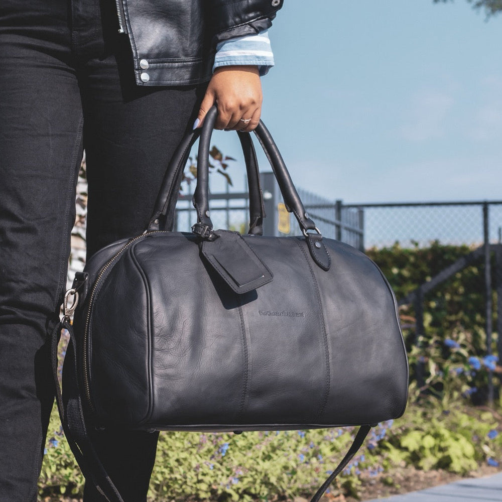 Person holding a black leather duffel bag outdoors.