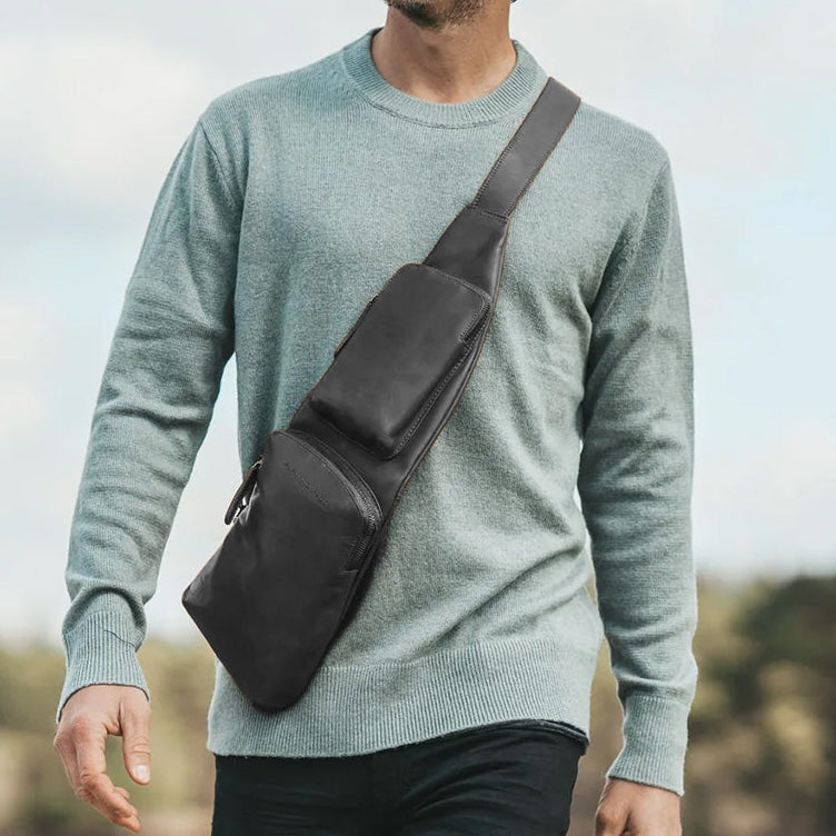 Man walking outdoors with a black sling bag, smiling