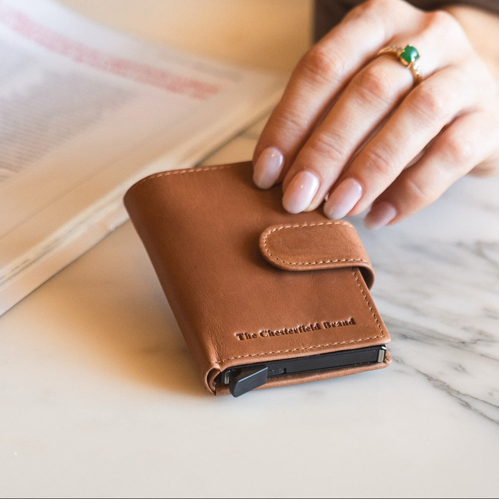 Cognac leather wallet with 'The Chesterfield Brand' logo on a marble surface.