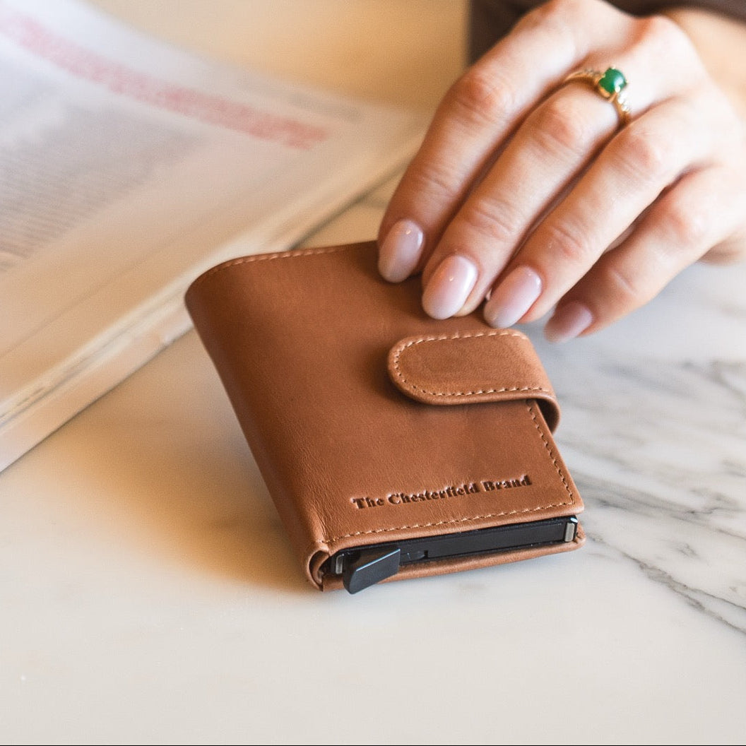 Cognac leather wallet with 'The Chesterfield Brand' logo on a marble surface.