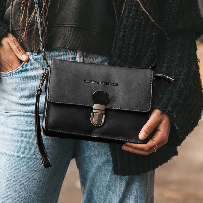 Person holding a black leather bag with a blurred background