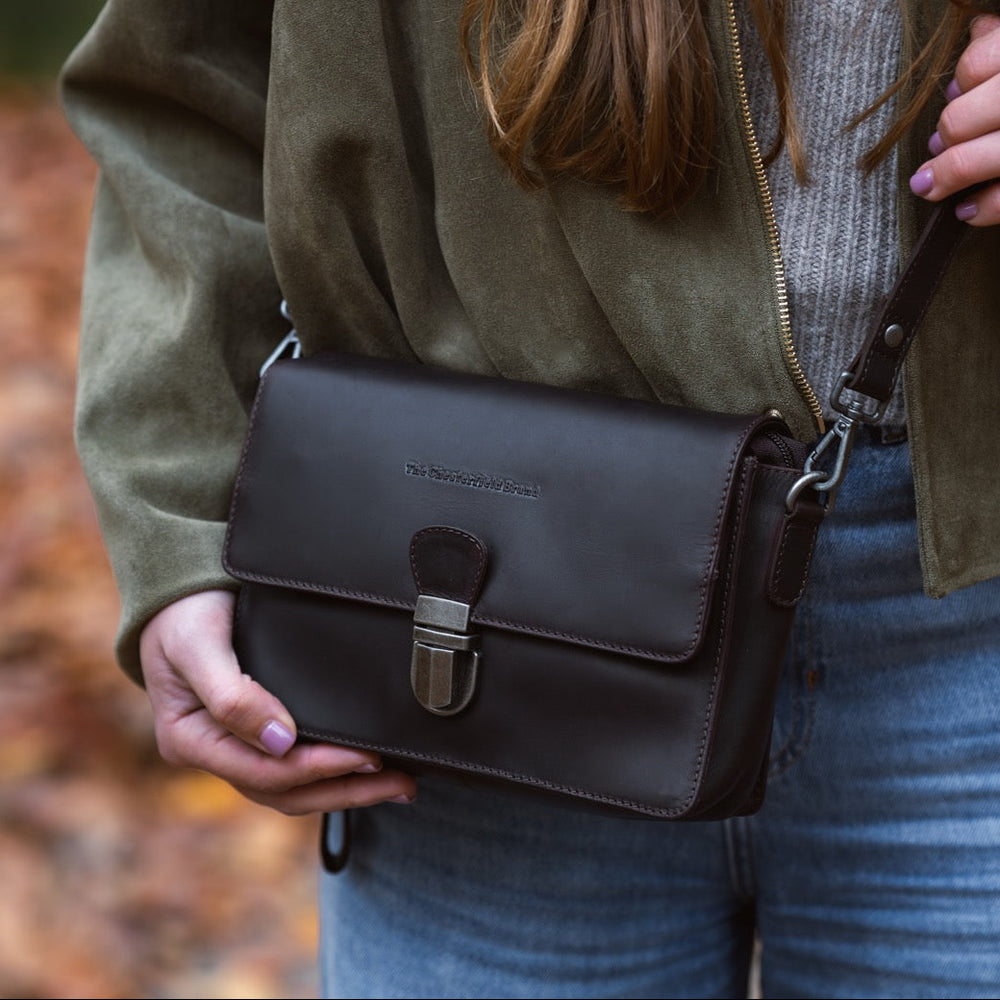 Person holding a brown leather bag outdoors with a blurred natural background