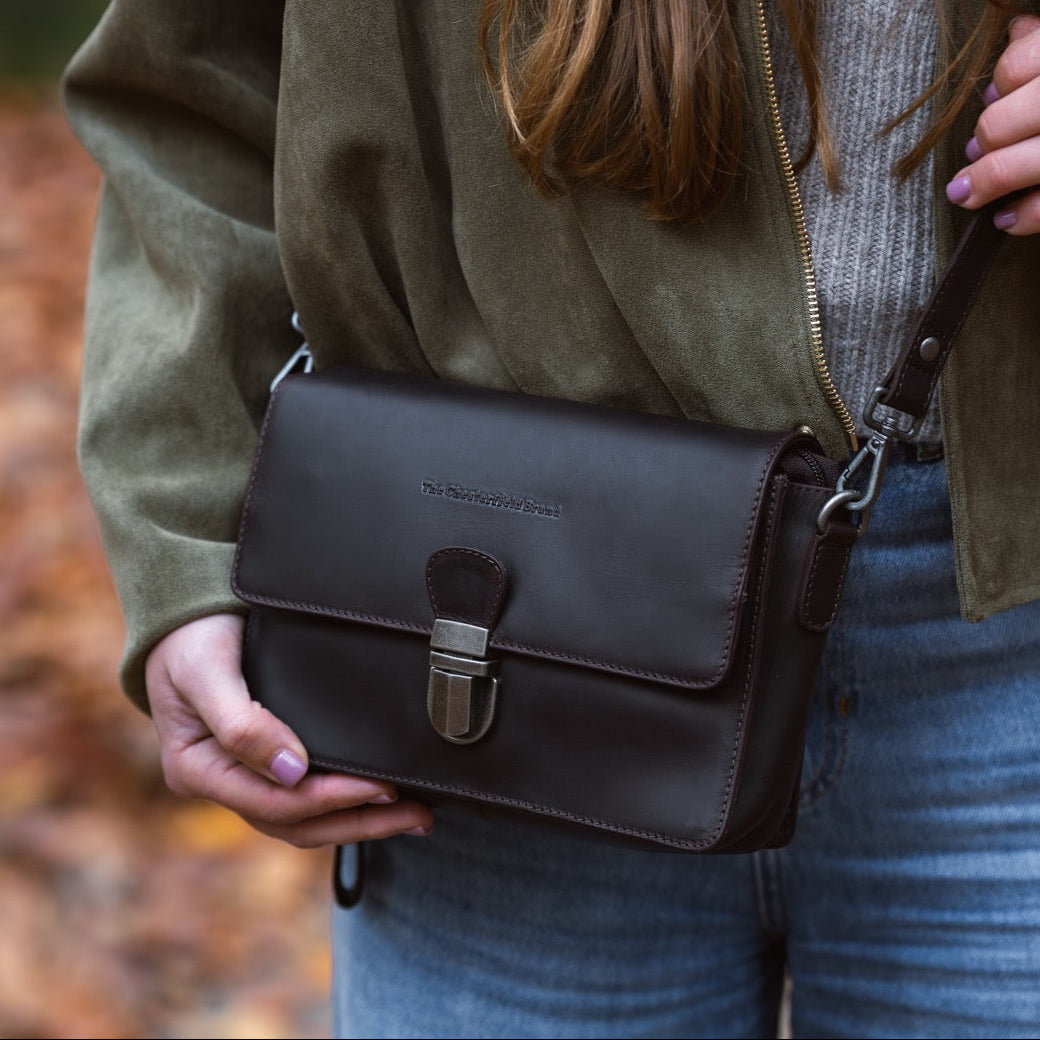 Person holding a brown leather bag outdoors with a blurred natural background