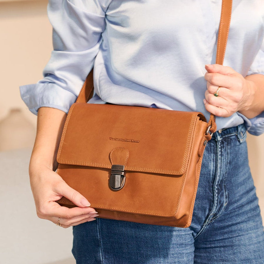 Person holding a cognac leather satchel bag against a neutral background