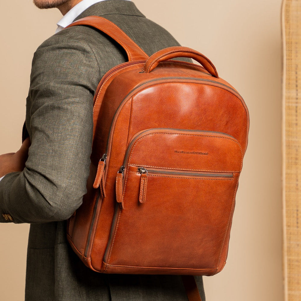 Man wearing a cognac leather backpack against a beige background