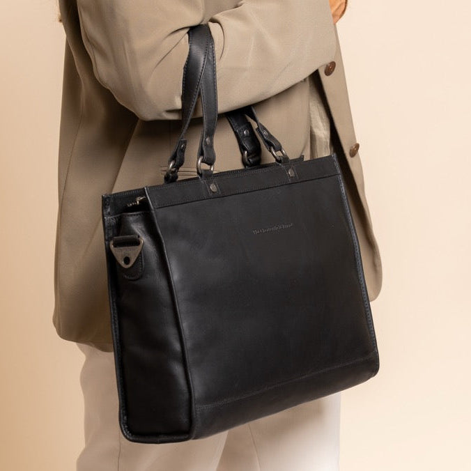 Woman holding a black leather bag against a beige background